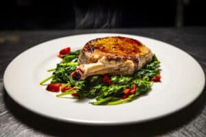 Juicy grilled pork chop served on a bed of fresh spinach and cherry tomatoes.