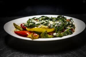 Delicious vegetable pasta with fresh greens, peppers, and cheese on a white plate. Perfect for healt.