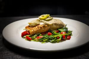 Grilled fish fillet with green vegetables and cherry tomatoes on a white plate.