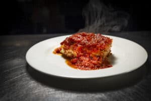 Hot steaming meat lasagna with rich tomato sauce on a white plate.