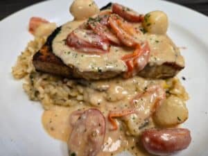 Juicy grilled pork chop topped with creamy mushroom sauce and vegetables.
