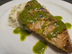 Delicious grilled fish topped with vibrant green herb sauce, served with a side of rice. Perfect for.