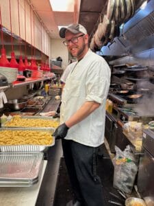 Chef in a restaurant kitchen preparing fried food with a smile.