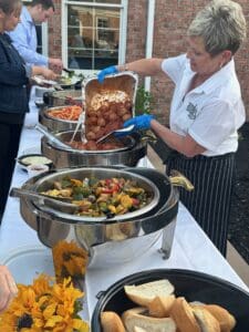 Buffet with assorted vegetables, fried chicken, and bread rolls served outdoors.