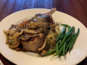 Delicious grilled lamb chops with mushroom sauce and fresh green beans on a white plate.