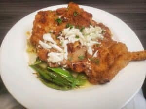Fried chicken with crab meat topping served with green vegetables on a white plate.