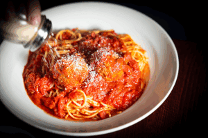Spaghetti with tomato sauce and meatballs, topped with grated cheese, served in a white bowl.